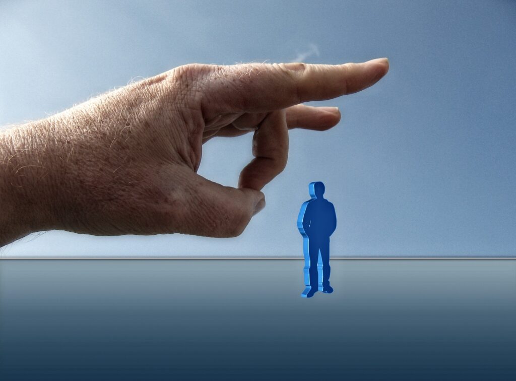 A little blue man about to be plinked away by a giant hand
